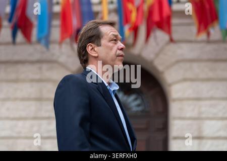 Selbstbewusster reifer Mann in einer Geschäftsjacke, der neben einem Gebäude mit internationalen Flaggen steht Stockfoto