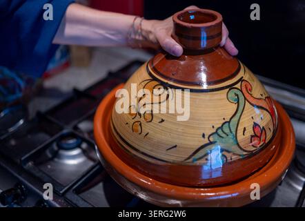 Heben Sie den konischen Deckel von der Hand aus einem Topf, um ein traditionelles marokkanisches Gericht auf einem Herd mit Hühnchen, Kartoffeln und Oliven zuzubereiten Stockfoto