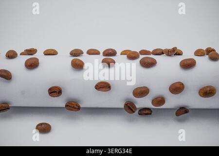 Abstraktes Kaffeebohnenmuster, das eine weiße Struktur vor einem verschwommenen Hintergrund aufsteigt. Stockfoto