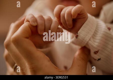 Erwachsene Mutter, die zu Hause Kinderhände hält Stockfoto