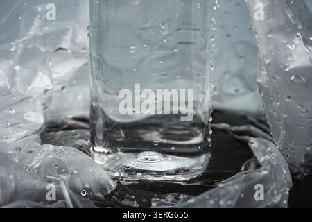 Durchsichtige Wasserflasche aus Kunststoff mit Tropfen, die auf zerknittertem Cellophanpapier liegen Stockfoto