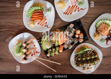 Fünf weiße Teller mit Sushi, Sashimi, Brötchen. Teller angeordnet Tisch Essstäbchen. Konzentriere dich auf leuchtende Farben und Texturen. Idealer Lebensstil, Stockfoto