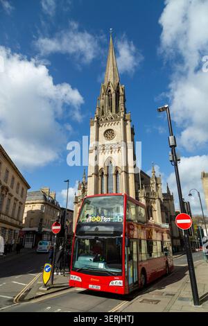 Ein Tootbus Bath mit offenem Oberdeck vor der St. Michael's Church, einer Kirche im gotischen Stil aus dem 19. Jahrhundert, Bath, Somerset. Stockfoto