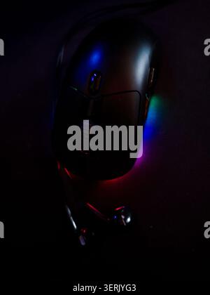 Ein ästhetisches Bild einer schwarzen ergonomischen Gaming-Computermaus aus bei schlechten Lichtverhältnissen mit lebendiger RGB-LED-Beleuchtung auf einem schwarzen Mousepad. Stockfoto