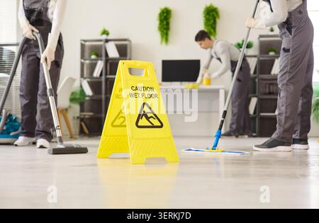 Reinigungsteam wischt den Büroboden mit Warnschild und Vakuum im Hintergrund Stockfoto