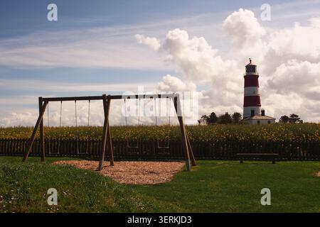 Ein Blick auf den Leuchtturm in Happisburgh, Norfolk, England UK mit seinen weißen und roten Streifen, vom Spielpark aus, vor einem bewölkten Himmel Stockfoto