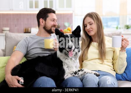 Glückliches Paar trinkt Kaffee und ruht sich mit seinem Hund zu Hause auf dem Sofa aus Stockfoto