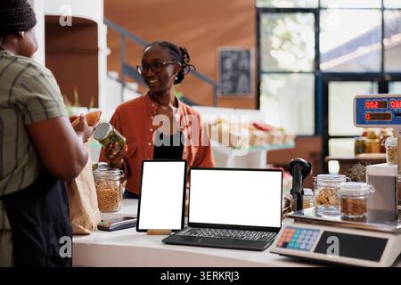 Kunden kaufen an der Kasse im Supermarkt chemikalienfreie Produkte ohne Abfall, während digitale Geräte einen isolierten weißen Bildschirm anzeigen. Stockfoto