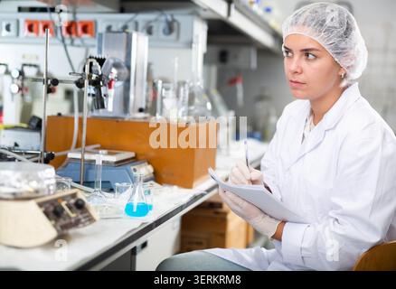 Junge Labortechnikerin, die arbeitet, Notizen schreibt Stockfoto