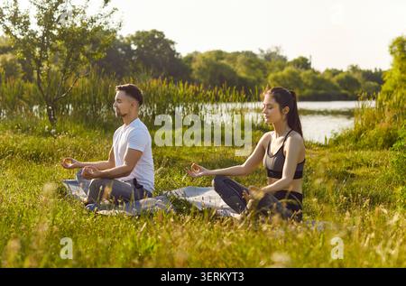 Yogi-Leute, die im Lotus sitzen, posieren draußen auf grünem Gras, meditieren, beruhigen Aktivitäten Stockfoto