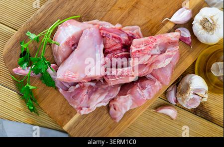 Roh geschnittenes Kaninchen, das auf einem Holzschneidebrett mit Gewürzen liegt Stockfoto