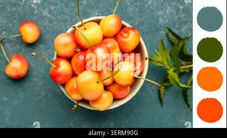 Frische rainier Kirschen in weißer Schüssel mit Minzzweig auf dunklem Petrol Hintergrund, gesunder Sommer Obst Snack, die süßen und Reifen Früchte bieten ein gesundes an Stockfoto