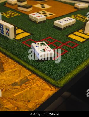 Eine Nahaufnahme, die ein Paar traditioneller Mahjong-Blumen- und Saisonsteine zeigt, die mit der Vorderseite nach oben auf einer grünen Filzmatte platziert werden, während andere Spielsteine auf Akro verstreut sind Stockfoto