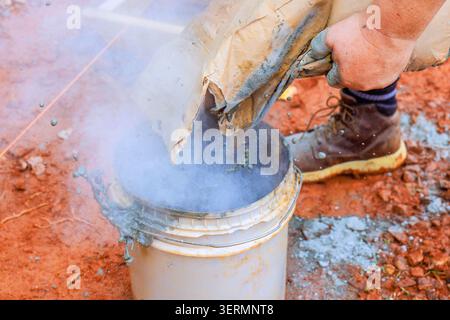 Auf der Baustelle wird eine trockene Mischung in den Eimer gegossen, während Rauch austritt. Staub ist auf dem Boden vorhanden. Stockfoto