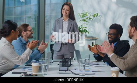 Weiße Führungsfrau mit einem Dokument, das mit dem Geschäftsteam spricht und bei der Bürositzung applaudiert. Erfolgreiche Geschäftsfrau spricht mit Führungskollegen Stockfoto