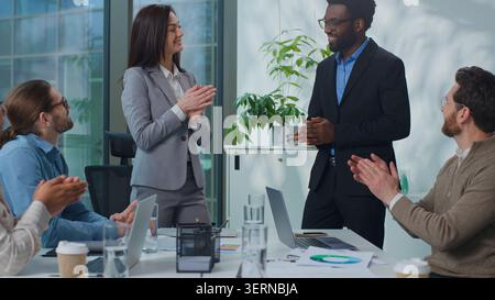Kaukasische Cheffrau lädt einen afroamerikanischen Mann ein, der neue Arbeiter in ein multiethnisches Geschäftsteam bei einer Bürositzung präsentiert. Geschäftsfrau Recruiterin Stockfoto
