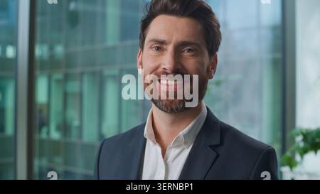 Nahaufnahme kaukasischer erwachsener Geschäftsmann lächelnd glücklich mit gesunden Zähnen, der in die Kamera bei der Bankagentur blickt. Europäischer Geschäftsmann reifer männlicher Unternehmer Stockfoto