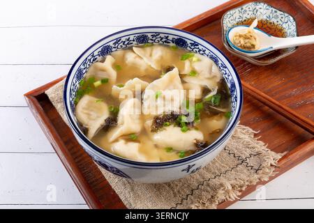 Chinesische Sauerknödel Jiaozi serviert in herzhafter Brühe mit Zwiebeln und Algen Stockfoto