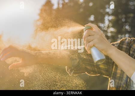 Nahaufnahme einer Frau, die draußen Insektenspray auf ihren Arm aufträgt. Sichtbarer Aerosolnebel, der durch Sonnenlicht beleuchtet wird. Konzept von Mücken und Zecken PR Stockfoto
