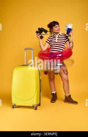 Eine selbstbewusste junge Frau lächelt, hält eine Kamera und wichtige Reiseutensilien in der Hand. Stockfoto