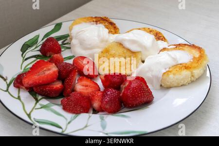 Traditionelles Syrniki-Frühstück mit süßen Beeren und weißer Joghurt-Creme Stockfoto