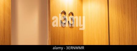 Apartmenttür Nummer 33 an einer modernen Holzpaneelwand montiert Stockfoto