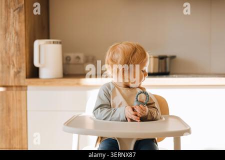 Kleinkind sitzt in einem Hochstuhl in einer modernen Küche zu Hause Stockfoto