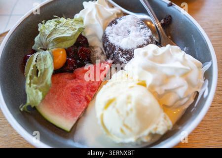 Ein köstliches Gourmet-Dessert, serviert in einer Schüssel mit Schokoladen-Lavakuchen, Vanilleeislöffeln, frischer Wassermelonenscheibe und Schlagsahne Stockfoto