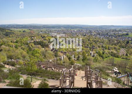 Weitwinkel-Panoramablick von einem hohen Hügel aus mit einem Outdoor Park Spielplatz, üppigen grünen Wald und einer europäischen Kleinstadt unter einem klaren Himmel Stockfoto