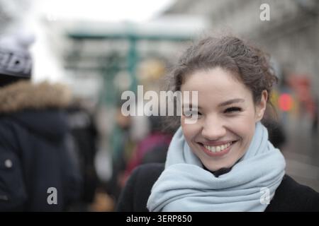 Glückliche junge Frau, die auf einer geschäftigen Straße lächelt Stockfoto