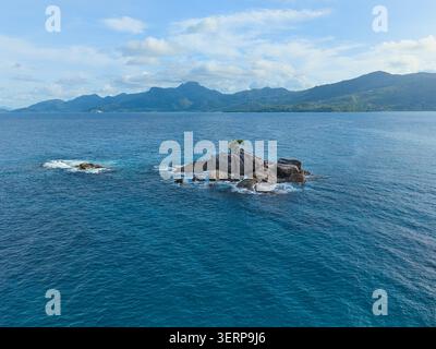 Luftbild eines einsamen felsigen Inselchens mit grünen Bäumen, umgeben von tiefblauem und türkisblauem Ozeanwasser, Anse solei, Mahe, Seychellen Stockfoto