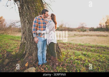 Ein romantisches Paar teilt sich einen Kuss draußen an einem Baum Stockfoto