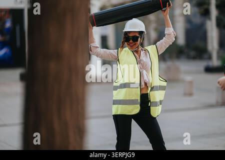 Bauarbeiterin in Schutzhelm und Weste, die draußen eine Blaudruckröhre hält Stockfoto