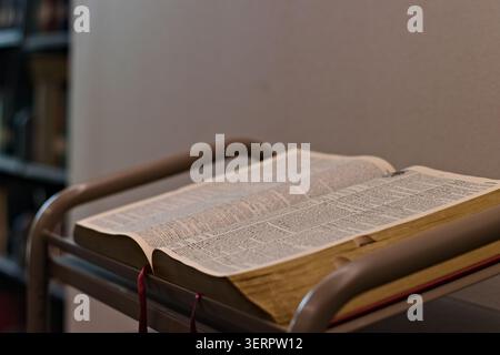 Offene Bibel, die auf einem Rednerpult der Kirche steht, steht in einem ruhigen Gotteshaus, das die Lektüre der Schriften, die Glaubensübung und die christliche Hingabe repräsentiert. Stockfoto