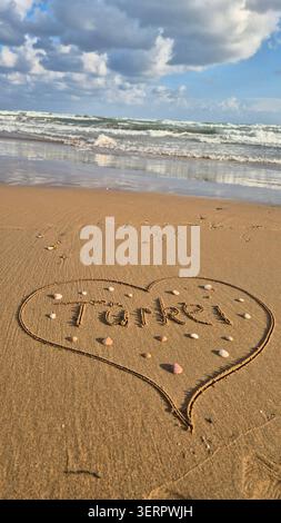 Herzform gezeichnet in Sand mit dem Wort Truthahn am Strand von Ocean Waves Stockfoto