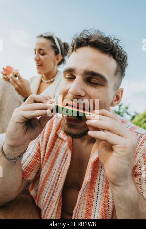 Junger Mann isst eine Wassermelonenscheibe draußen mit einem Freund an einem entspannten Sommertag Stockfoto