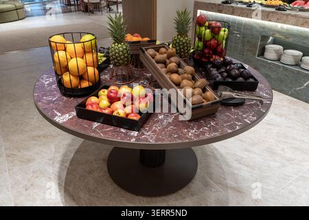 Eine reichhaltige Ausstellung verschiedener frischer ganzer Früchte in dekorativen Körben und Tabletts auf einem runden Marmortisch. Dieses Hotel-Frühstücksbuffet bietet OR Stockfoto