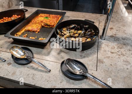 Eine Auswahl an warmen Gourmetgerichten in einem Hotelrestaurant vom Buffet mit frisch gekochten Muscheln in Soße und einem gebackenen Lasagna-Tablett. Selbstbedienungsservice Stockfoto