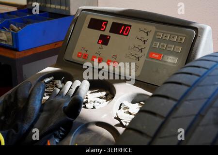 Nahaufnahme einer Radwuchtmaschine mit Reifen, Handschuhen und Radgewichten in einer Autowerkstatt Stockfoto