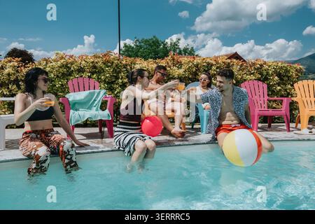 Freunde, die sich an einem sonnigen Sommertag bei einer Poolparty im Hinterhof bei Drinks und Strandbällen entspannen Stockfoto