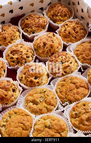 Frisch gebackene Muffins mit Samen in Papiereinlagen, dicht in einer weißen Box mit Herzmuster angeordnet. Stockfoto
