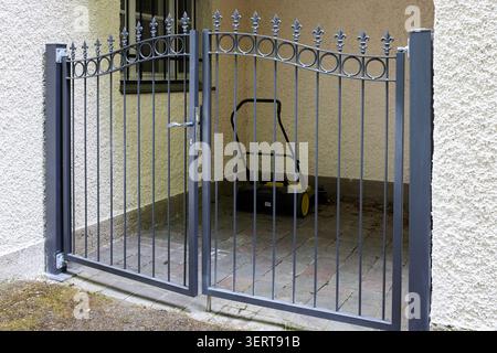 Schmiedeeisernes Tor mit dekorativen Elementen und einem Griff auf einer Betonterrasse im Hinterhof. Stockfoto
