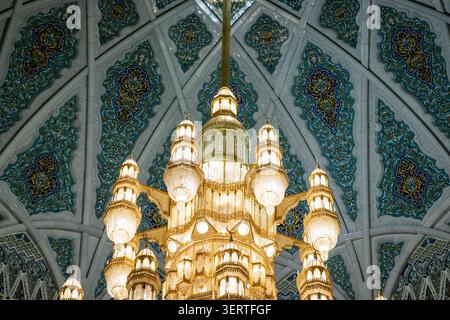 Blick auf den kunstvoll verzierten goldenen Kronleuchter, der von der aufwändig gekachelten Kuppeldecke in der Sultan-Qaboos-Moschee in Maskat, Maskat Governora, hängt Stockfoto
