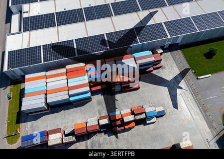 Luftaufnahme eines Frachtflugzeugschattens über einem nachhaltigen Containerterminal mit Solarpaneelen Stockfoto