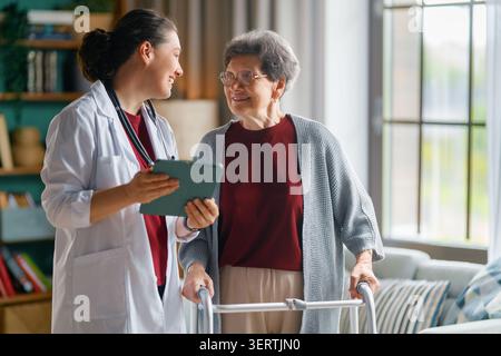 Eine herzerwärmende Szene mit einer mitfühlenden Ärztin, die eine ältere Frau mit einem Walker in einer gemütlichen häuslichen Umgebung unterstützt. Der Senior Patient A Stockfoto