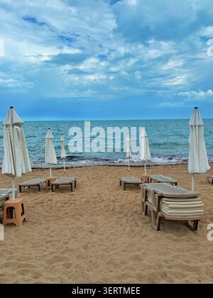Leerer Sandstrand mit geschlossenen Sonnenschirmen und Liegen vor Sturm Stockfoto