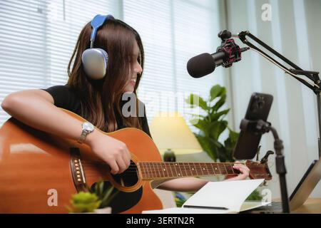 Asiatische junge Frau Influencer übt Akustikgitarre live, Musik Kommunikation Videoinhalte Laptop-Computer und Mobiltechnologie, Notizblock Stockfoto