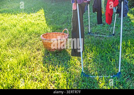 Farbige Wäsche trocknen auf einem Wäscheständer neben einem leeren Wäschekorb an einem sonnigen Tag Stockfoto