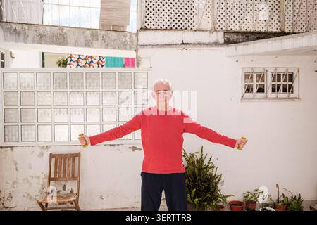Senior-Mann, der Bizeps-Curls mit Kurzhanteln durchführt und sich auf Wellness auf einer Terrasse konzentriert Stockfoto