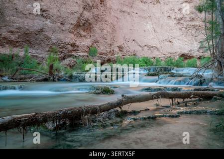 Blick auf die Havasu Falls mit türkisfarbenen Wasserkaskaden, die über Travertinterrassen gegen rote Felswände in Supai, Arizona, USA fließen. Stockfoto
